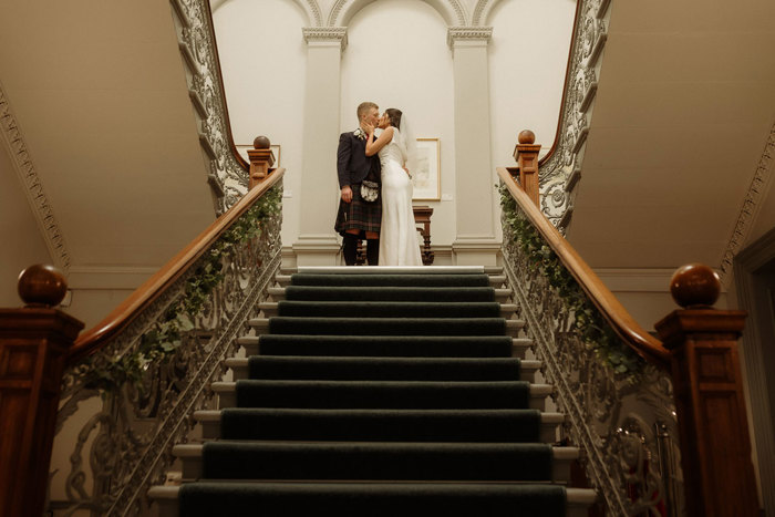 bride and groom kissing at top of staircase at kilmardinny house in bearsden