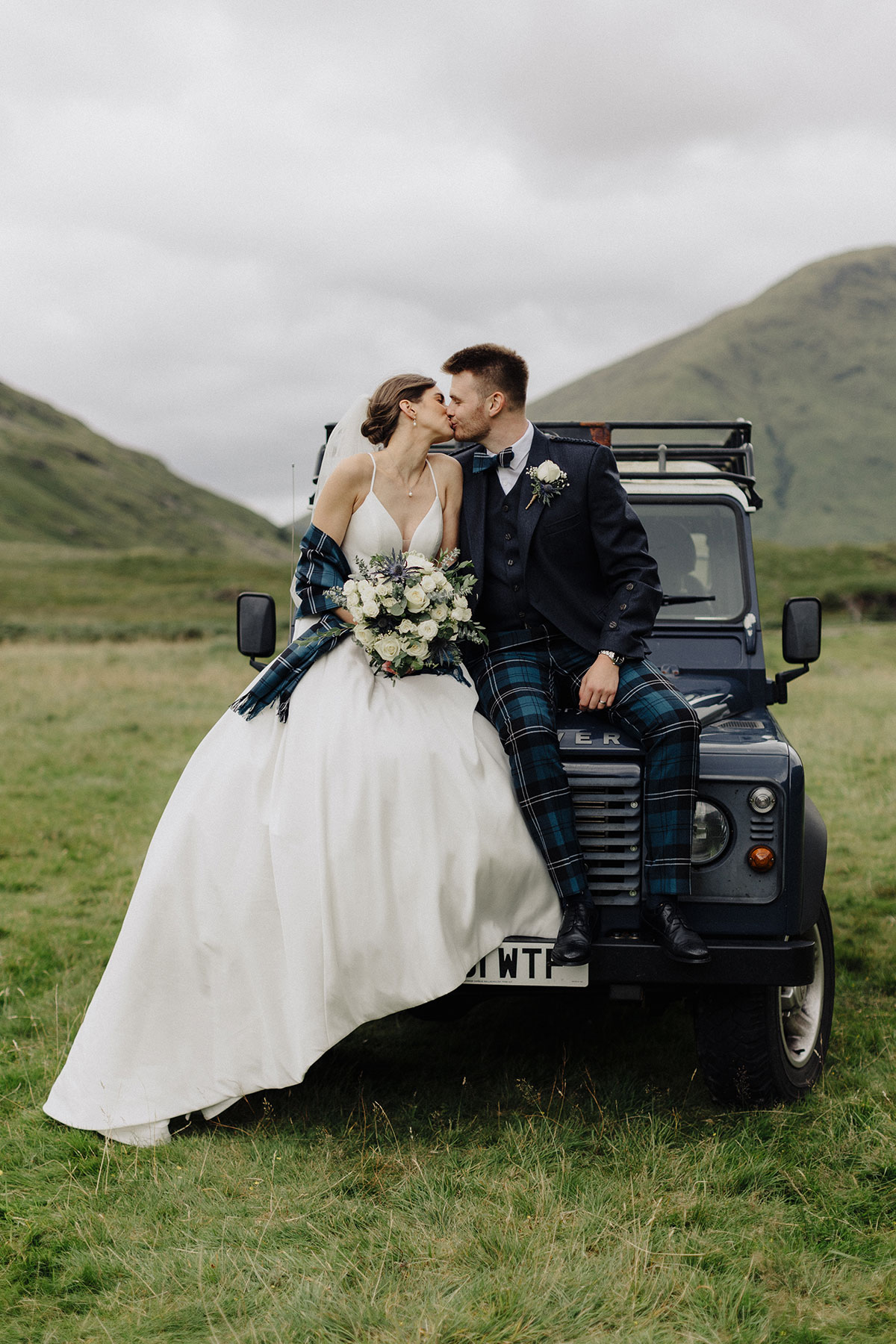 Bride and groom sharing a kiss on the hood of a landrover