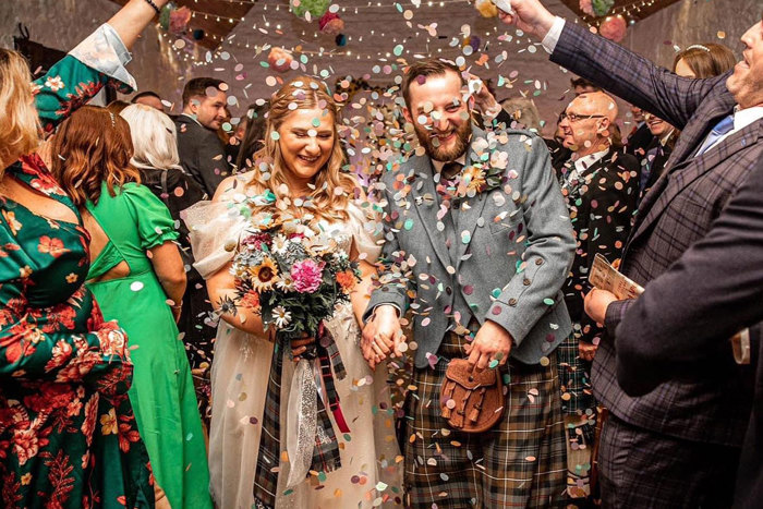 a couple walk through a crowd who throws colourful confetti over them