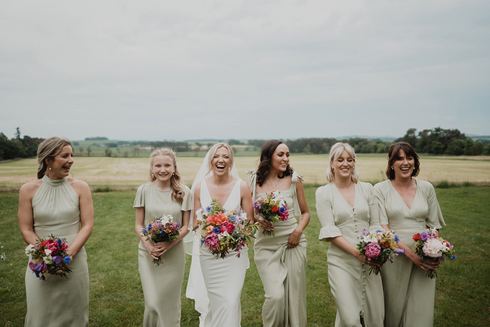 A Bride Walking In A Field With 5 Bridesmaids Wearing Pale Green Dresses