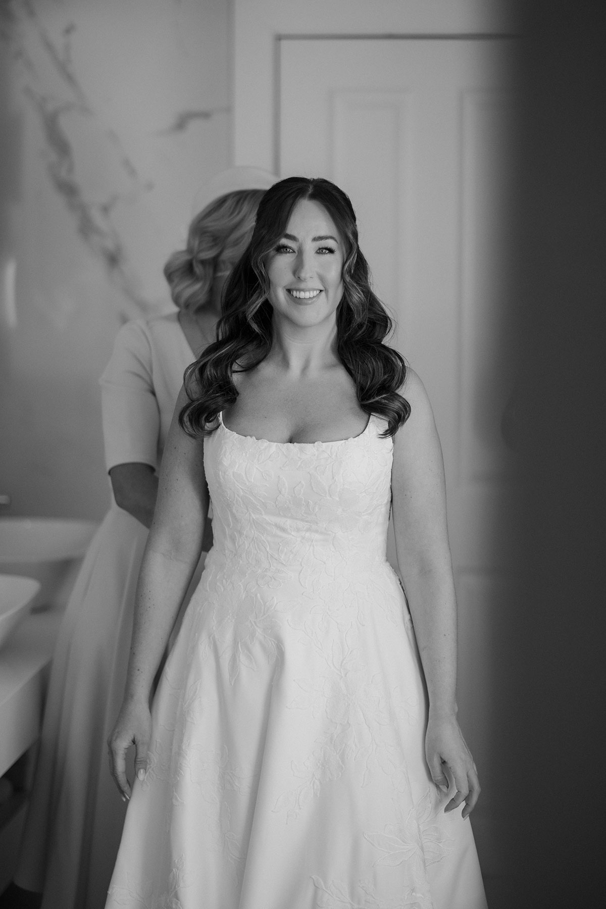a smiling bride with dark wavy hair wearing a square necked wedding dress