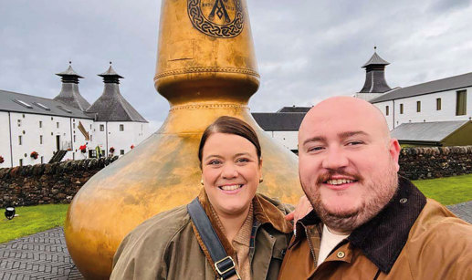 Two people standing in front of a large gold whisky still.