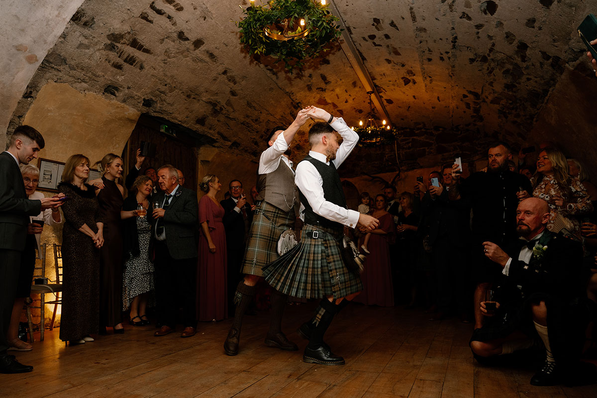 two grooms in kilts doing a first dance in a room at Neidpath Castle as guests watch on