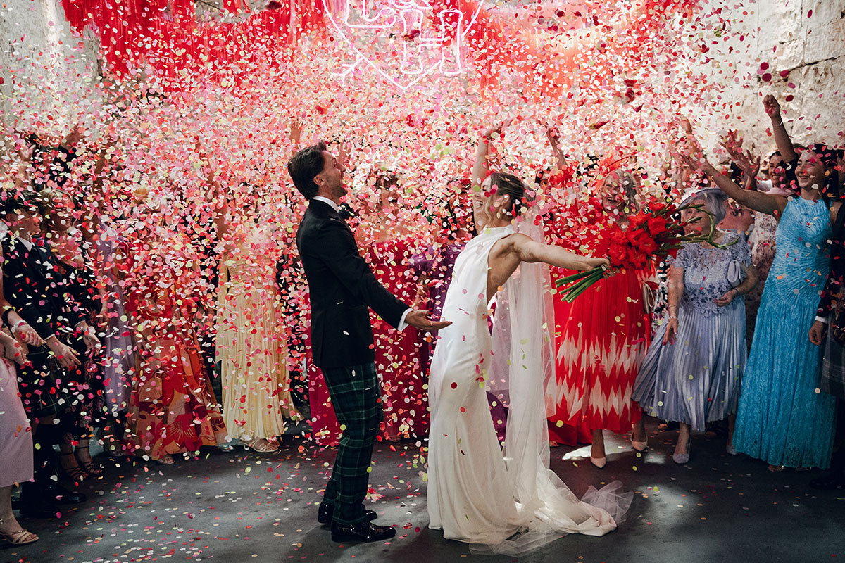 Bride and groom celebrate beneath a dramatic confetti cannon explosion surrounded by guests and colourful Mexican-inspired wedding décor at Kinkell Byre.