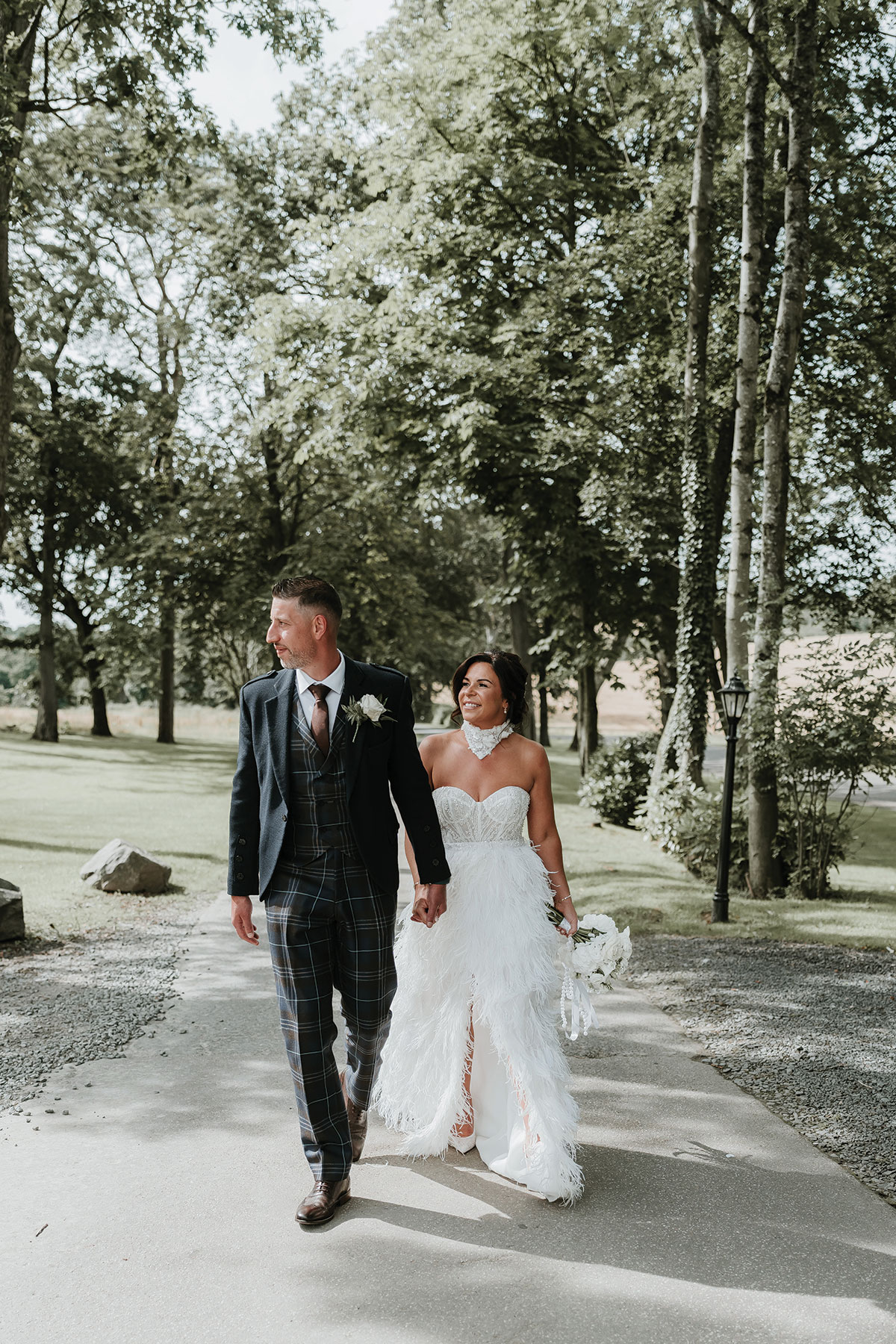 Bride wearing a bespoke strapless feathered wedding dress while walking outdoors with her groom.