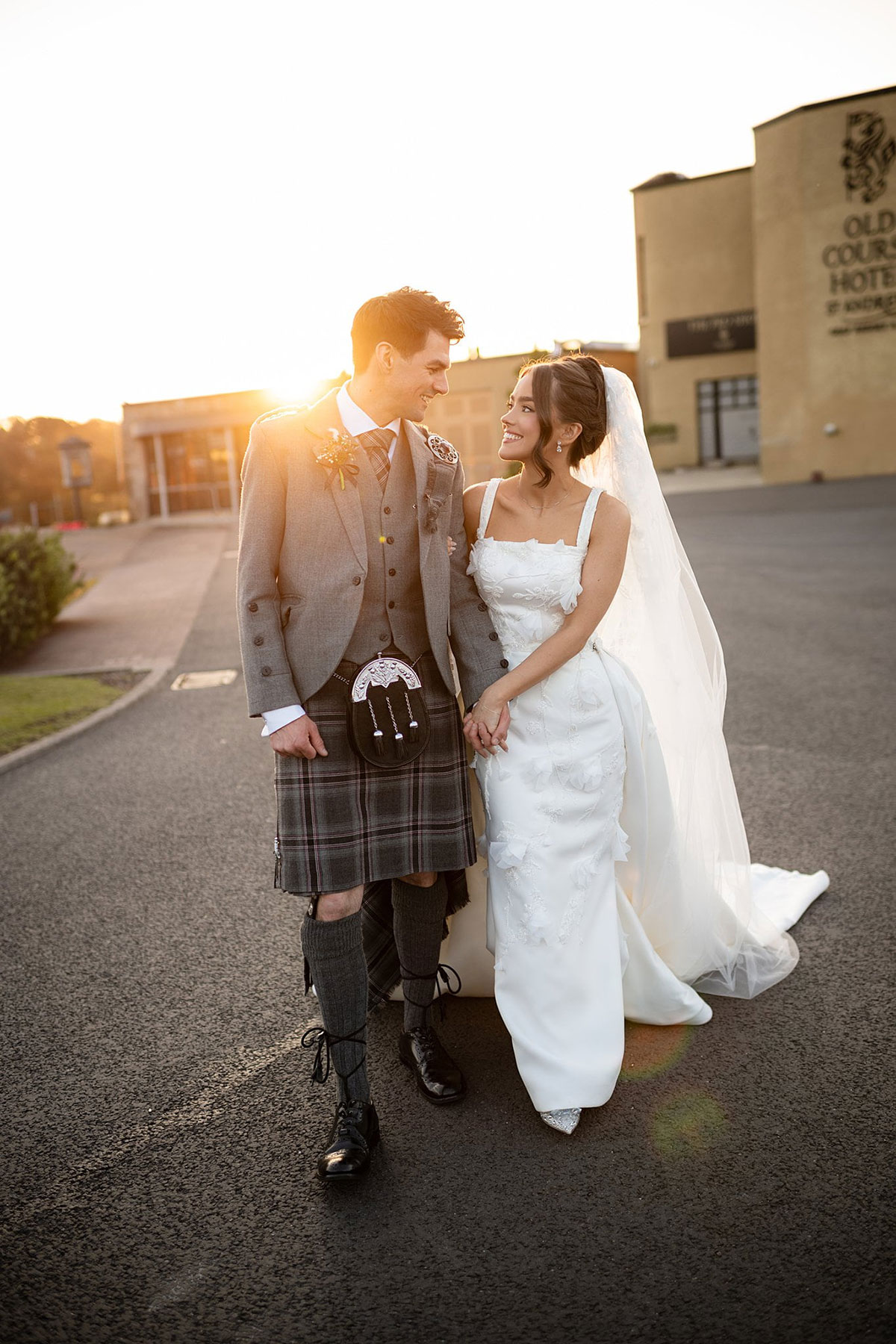 Bride and groom walking at sunset outside Old Course Hotel in St Andrews during elegant Scottish wedding.