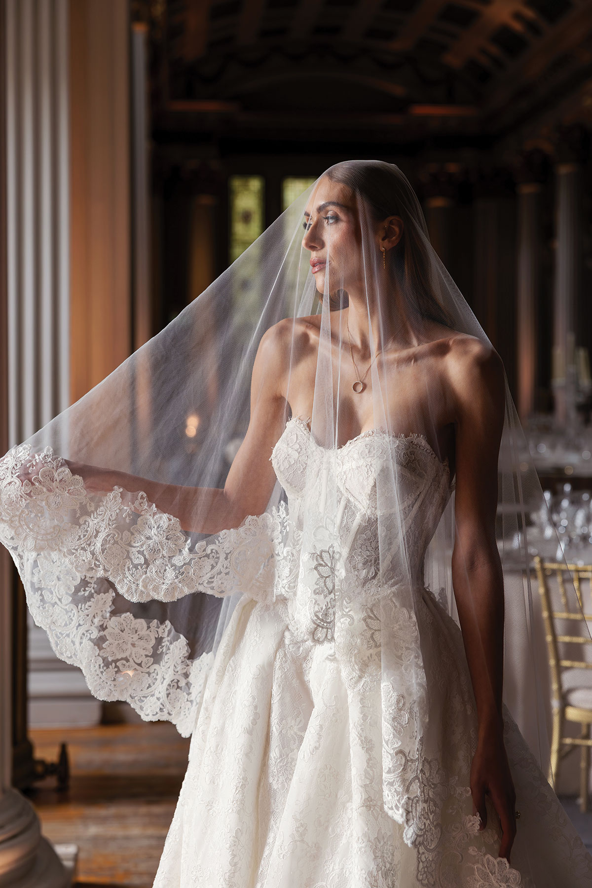 Bride in lace wedding dress and long veil standing in candlelit Signet Library ceremony space in Edinburgh