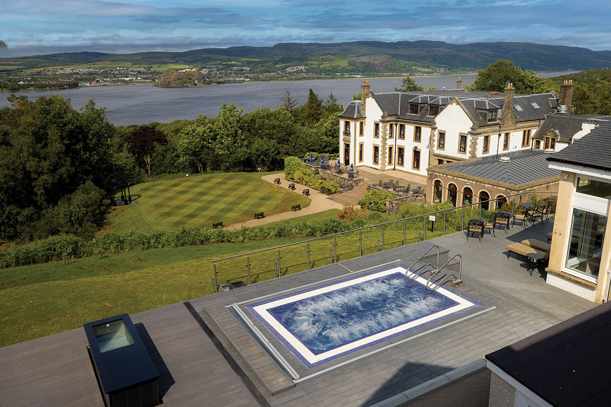 Outdoor swimming pool with bubbling water on a terrace overlooking manicured lawns, trees and a river valley beyond