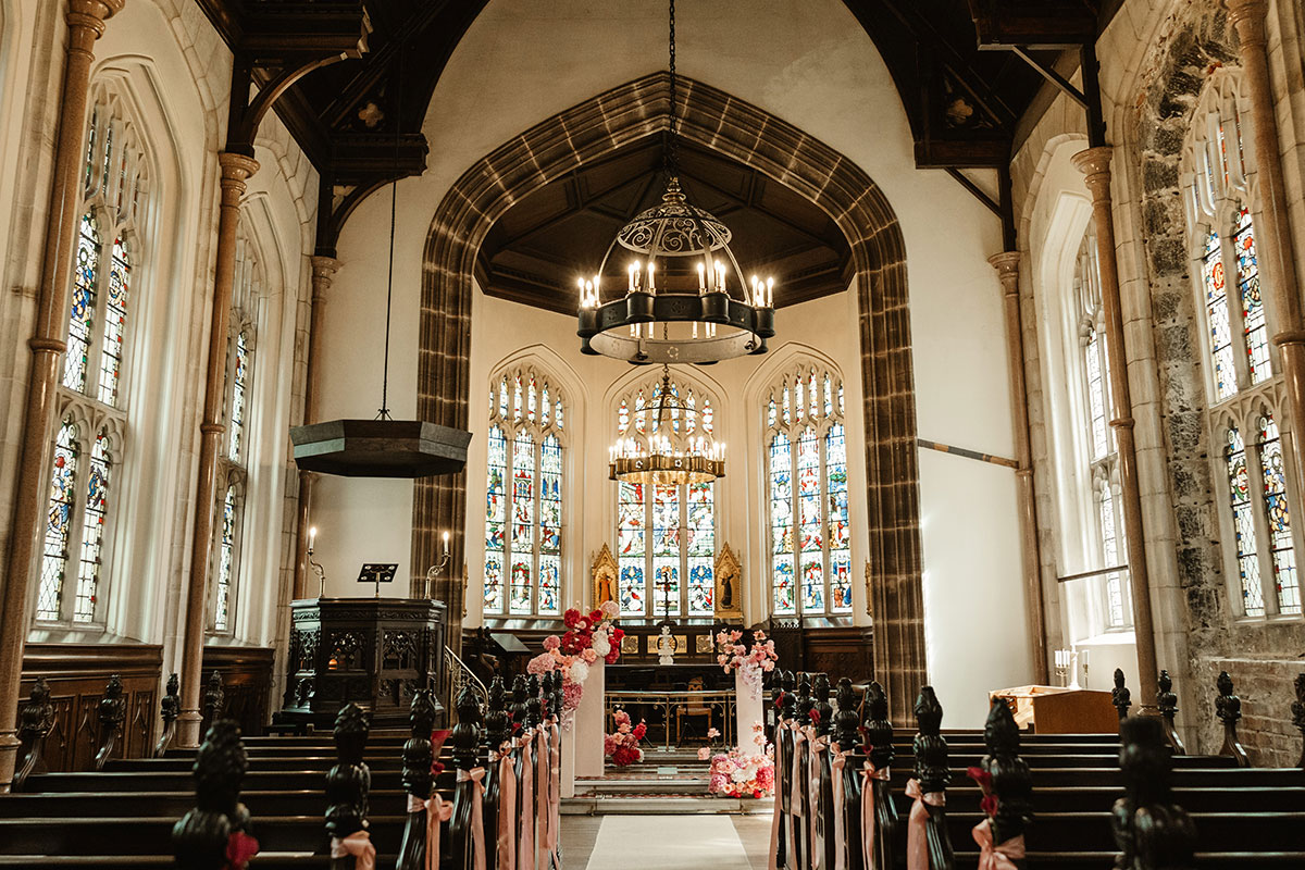 Historic chapel interior with stained-glass windows, chandeliers, and floral decorations along the aisle