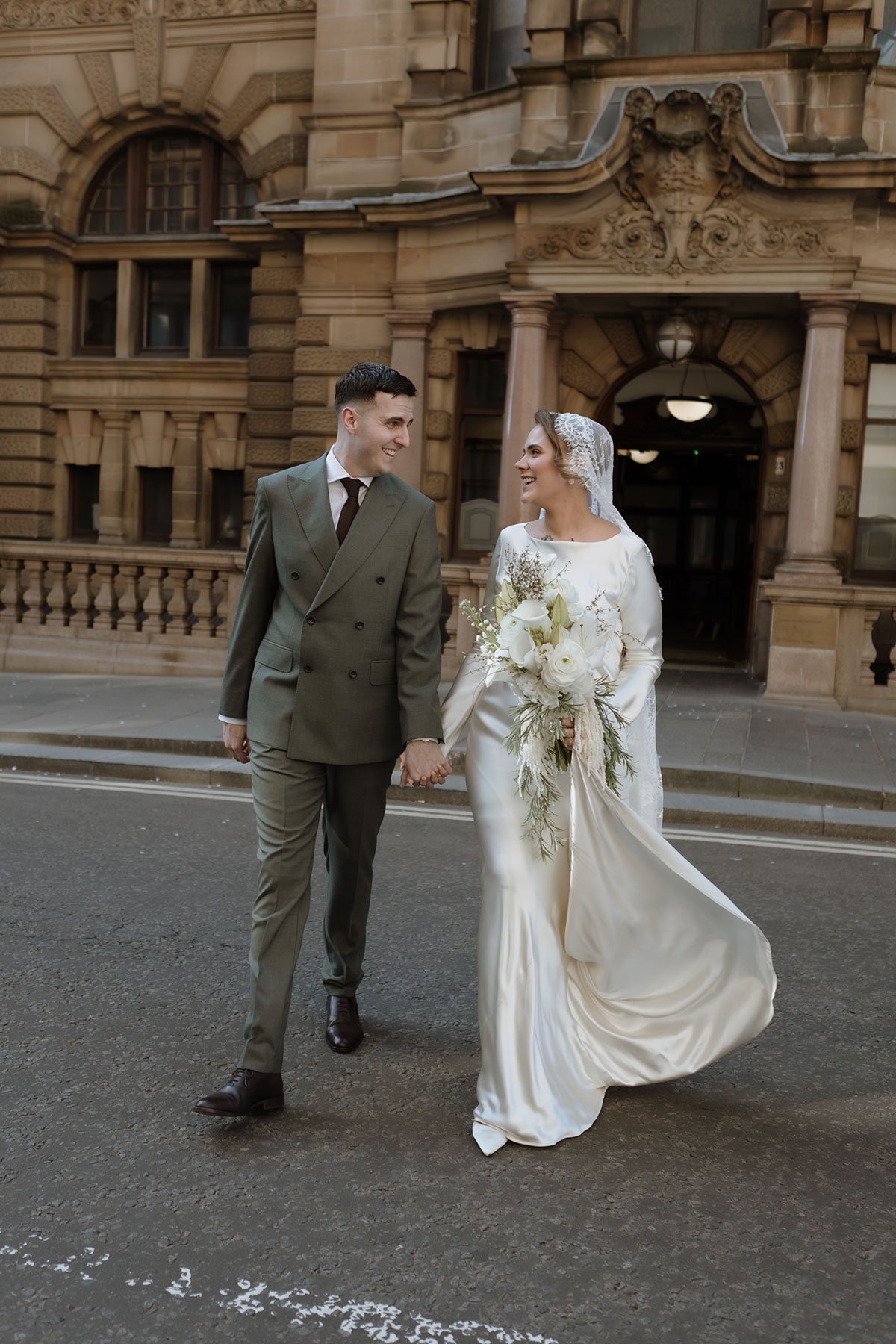 Newlywed couple walking hand in hand outside an ornate sandstone building during a Scottish city wedding