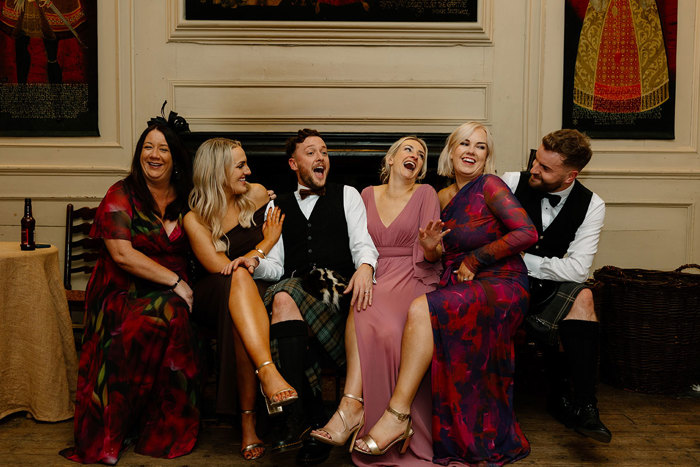 six people sitting down in a row during a wedding reception at Neidpath Castle