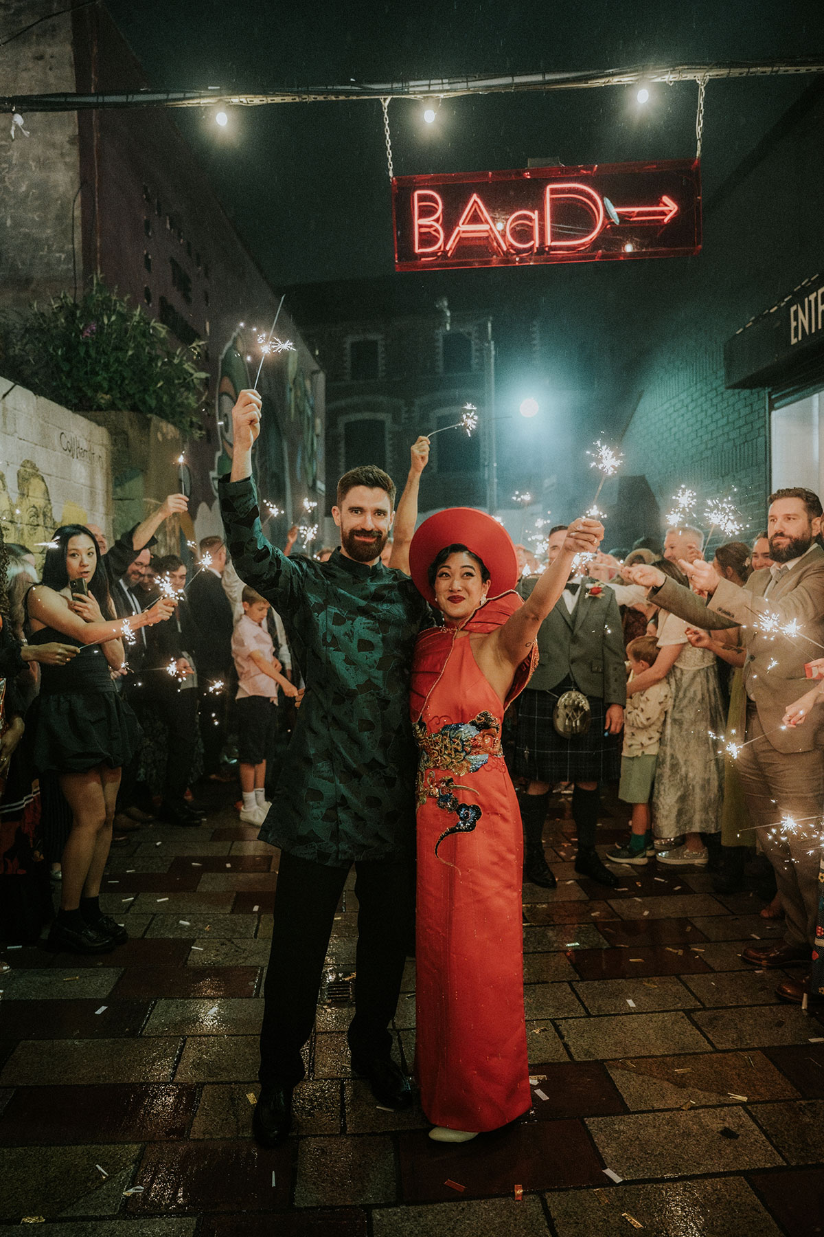 Bride and groom holding sparklers with guests outside BAaD Glasgow wedding venue at night
