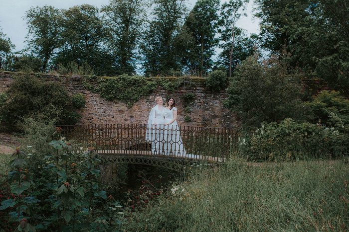 two brides stand on bridge in walled garden on wedding day at cambo house and estate