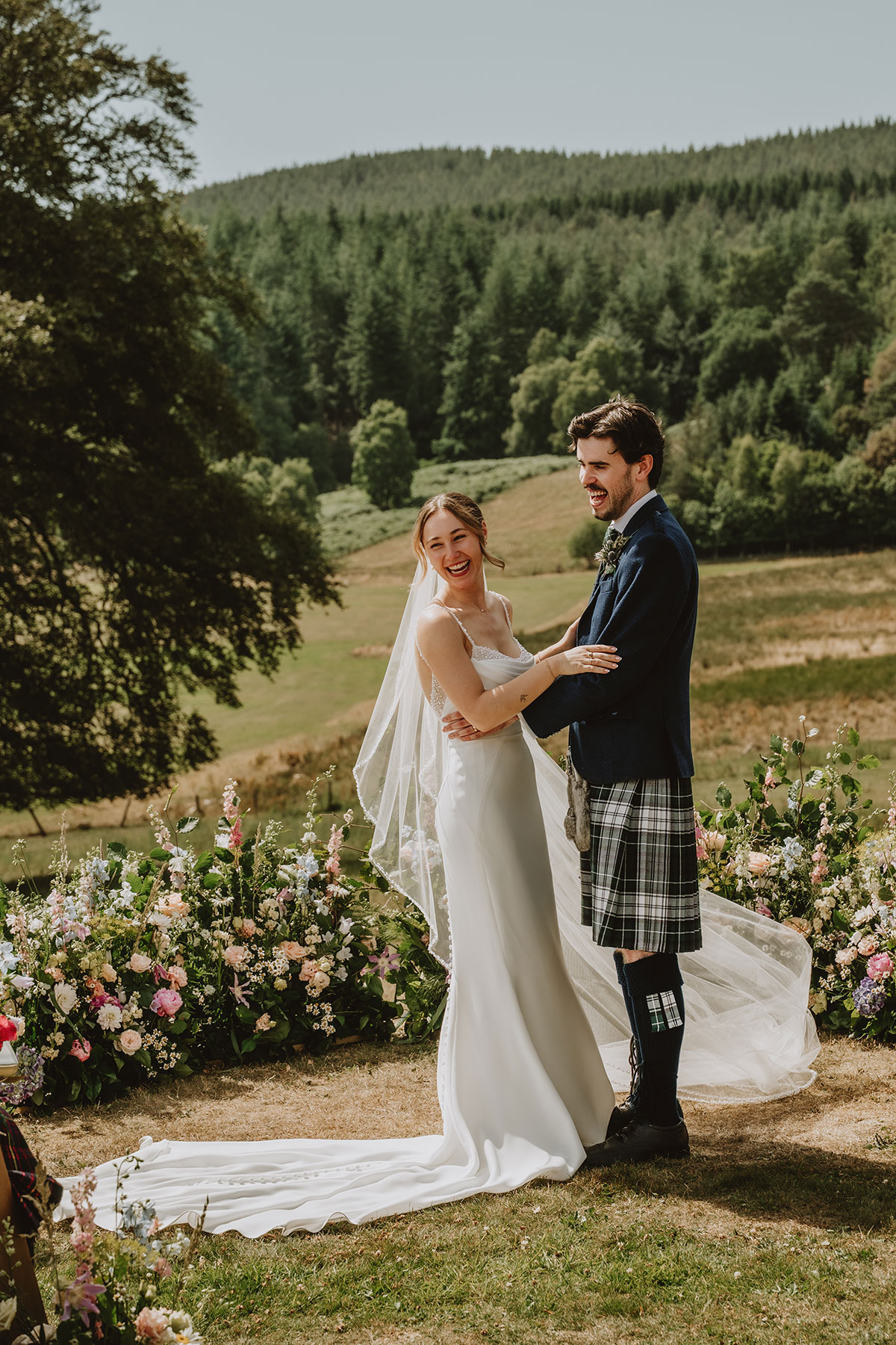 Bride and groom standing outdoors at Ballogie Estate with floral ceremony backdrop and countryside views