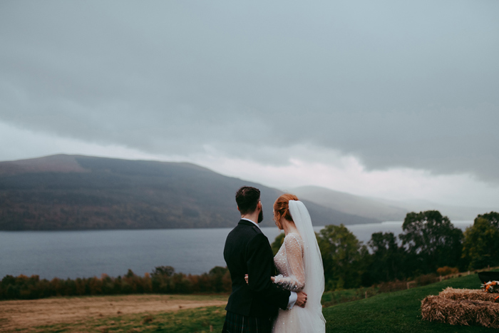 Bride and groom have back to the camera as they overlook loch and mountains