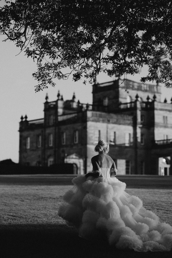 A bride wearing a wedding dress with a large skirt with several layers walking away from the camera towards a country house