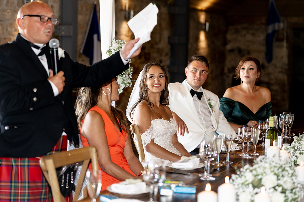 Father of the bride gives a heartfelt wedding speech at Falside Mill as the couple listen from the top table.