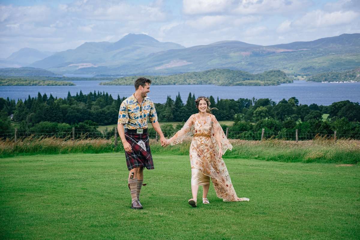 Couple walking hand in hand across the lawn at Ardoch Loch Lomond with loch and mountain views