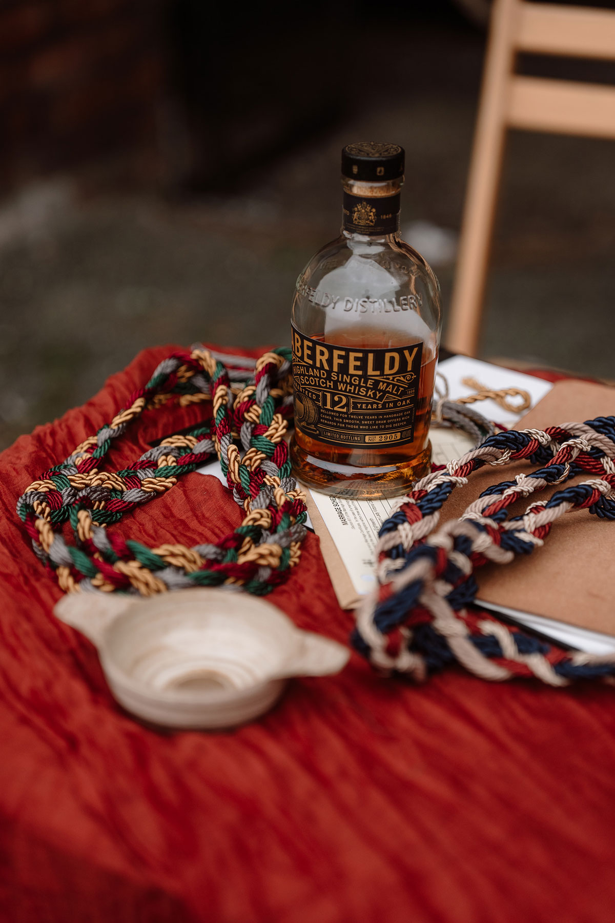 Bottle of Aberfeldy single malt whisky displayed alongside handfasting cords and ceremony details at a Scottish wedding celebration