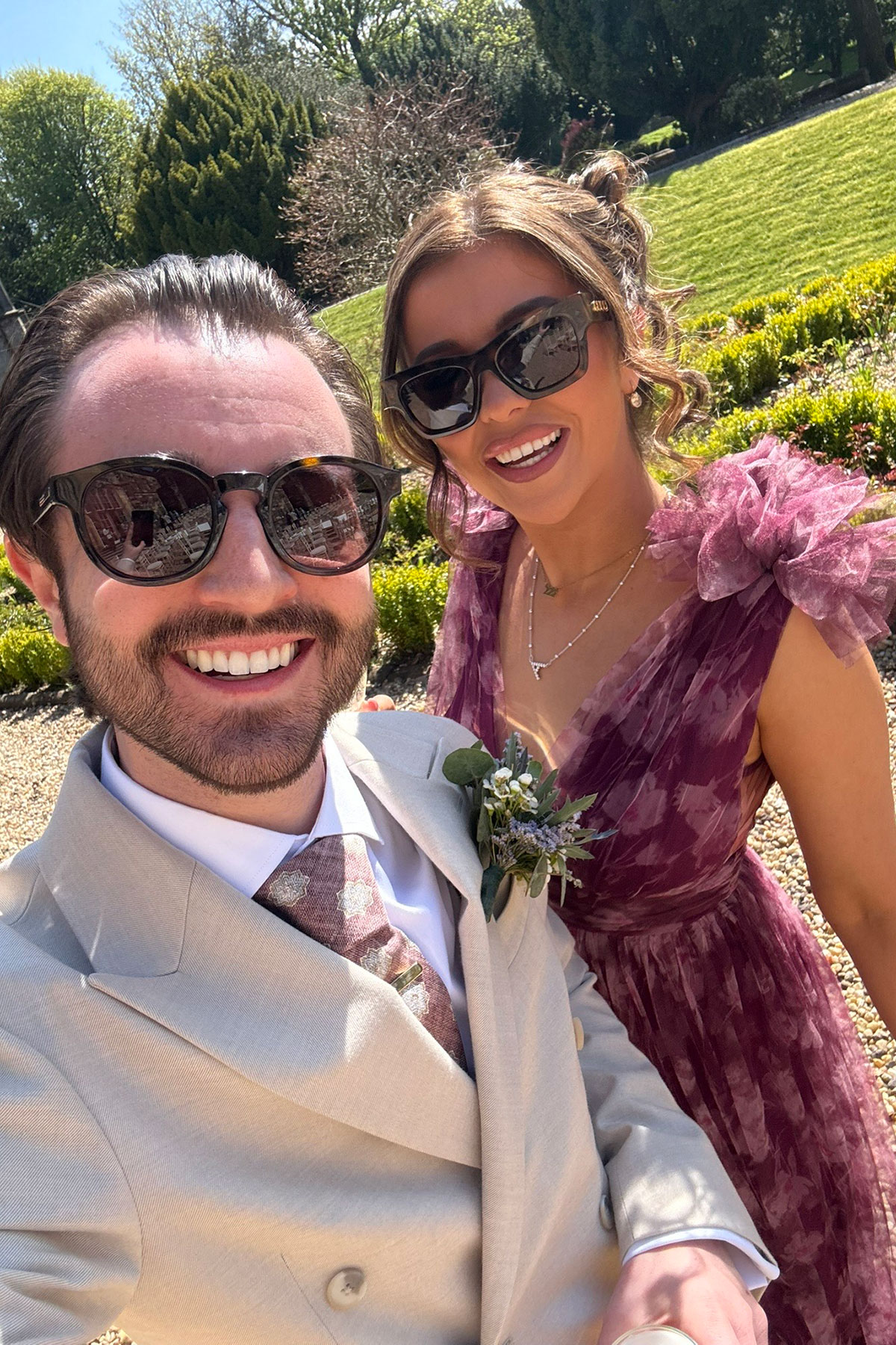 Wedding guest taking a selfie in sunglasses at a sunny Scottish castle wedding with formal gardens in the background