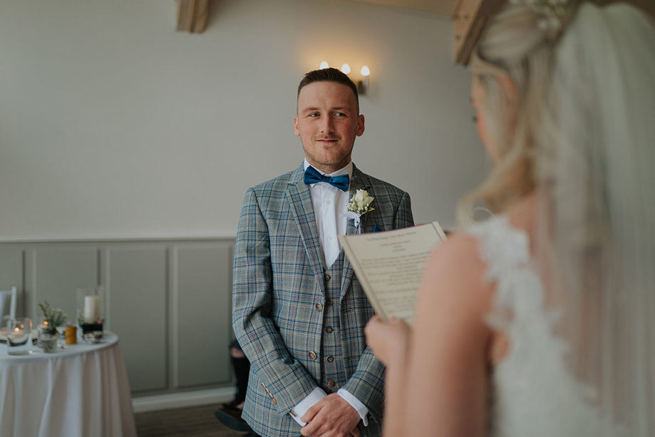 A Groom Stands With Hands Clasped And Looks Pensive As A Bride Reads From A Sheet Of Paper