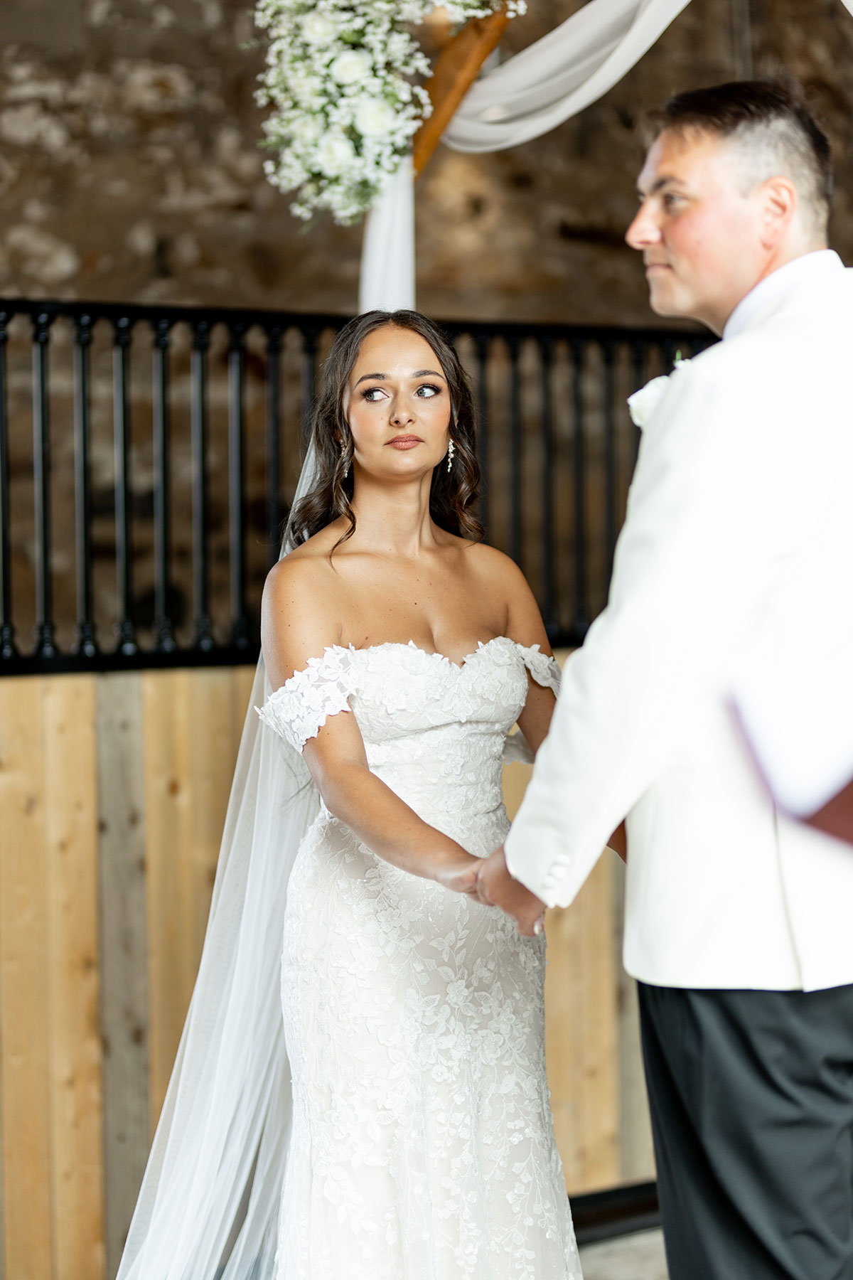 Bride and groom during a wedding ceremony at Falside Mill, holding hands under the floral-draped arch.