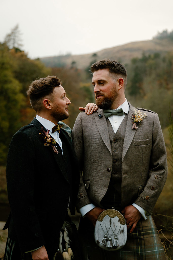 two grooms posing against autumn trees