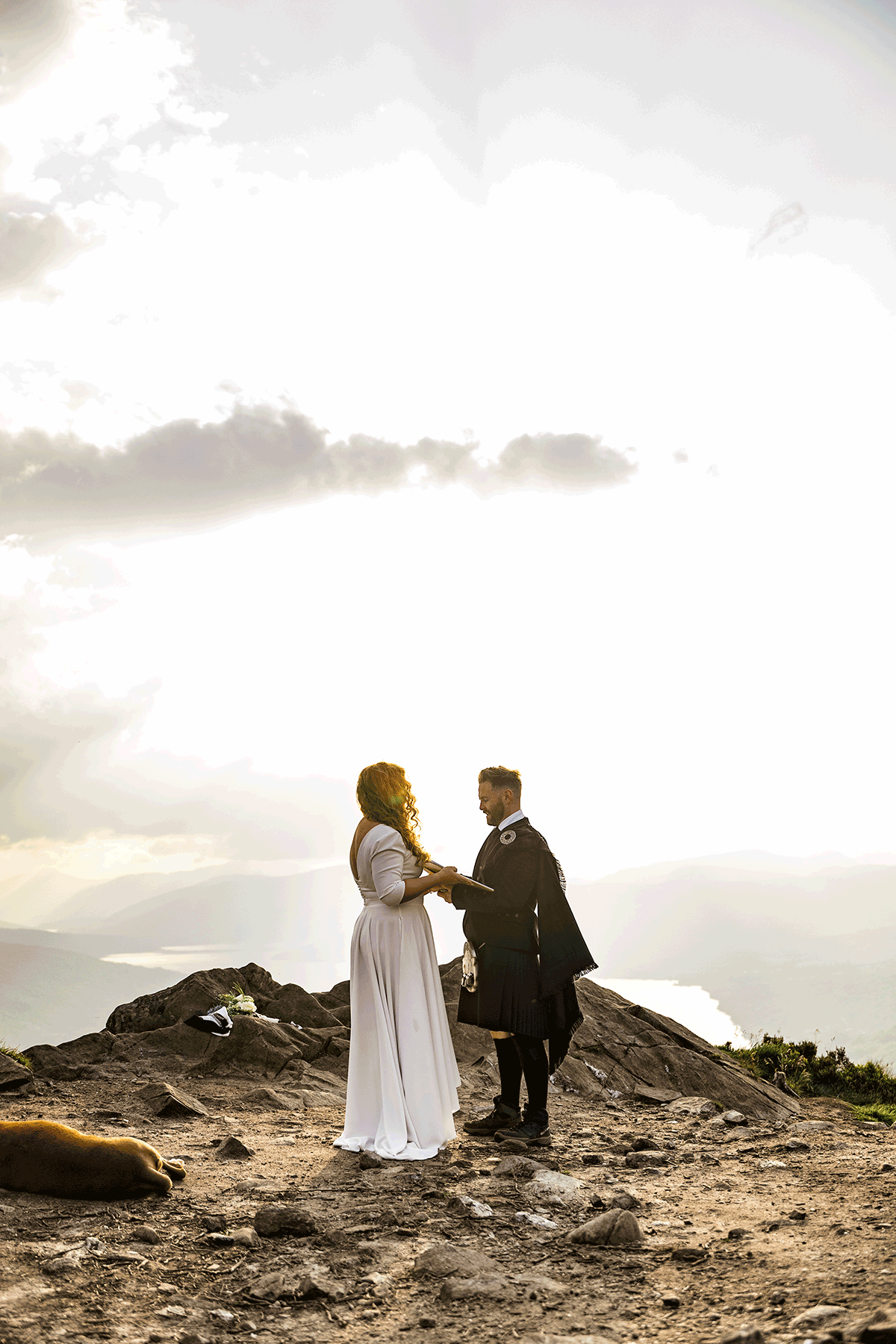 Bride and groom exchange vows on a rocky mountain summit with panoramic loch views and golden evening light