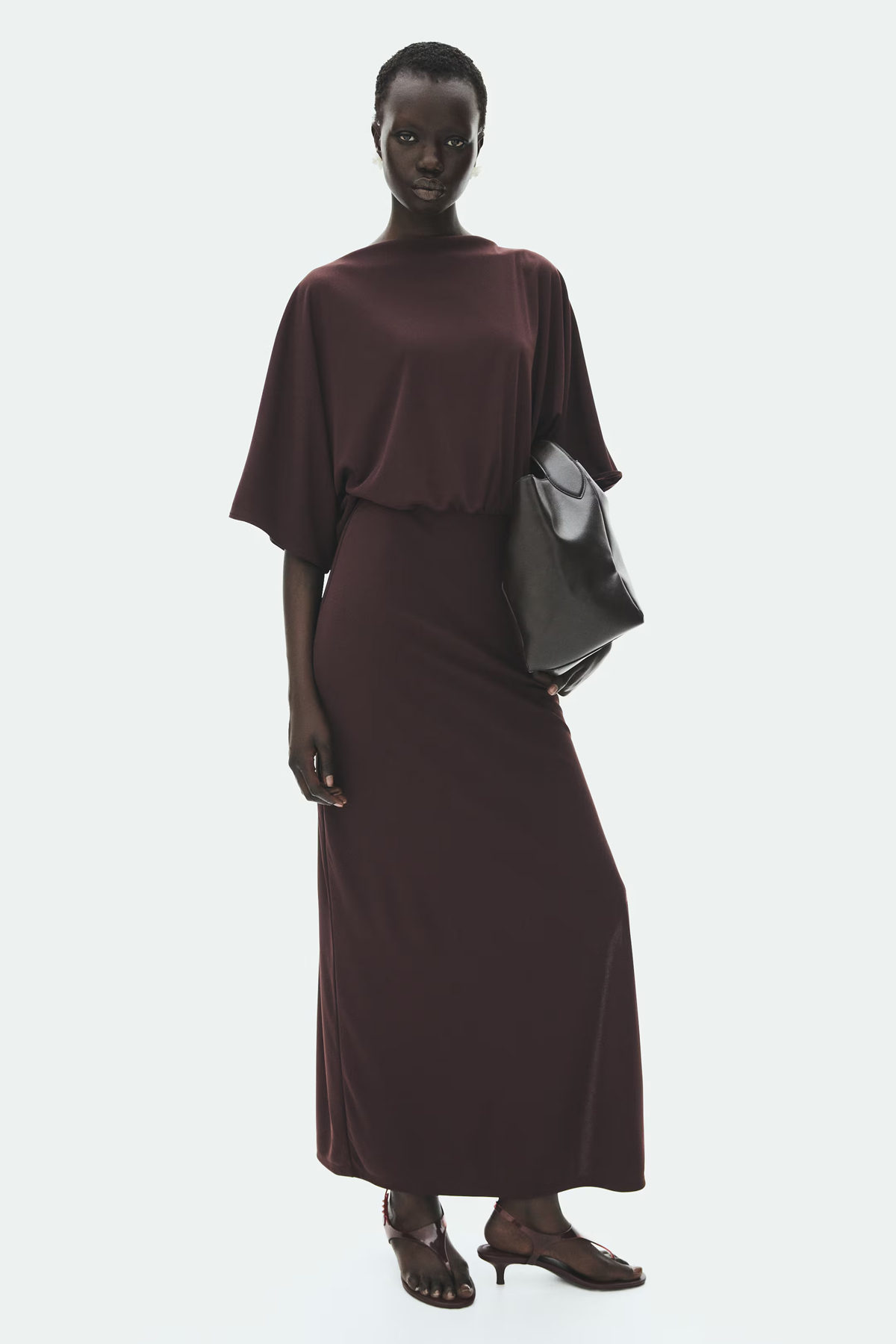 Model wearing a dark chocolate-brown jersey maxi dress with wide sleeves, a relaxed blouson bodice and flowing skirt.