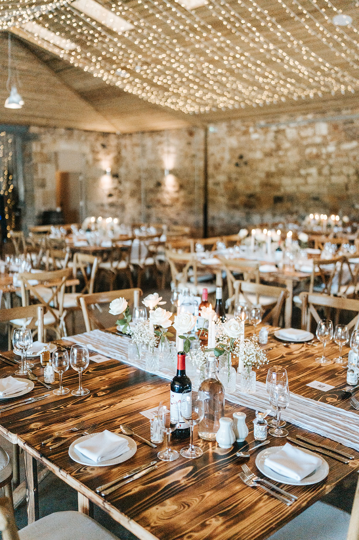 Rustic wedding reception tables with candles and fairy lights in a stone barn venue in Scotland