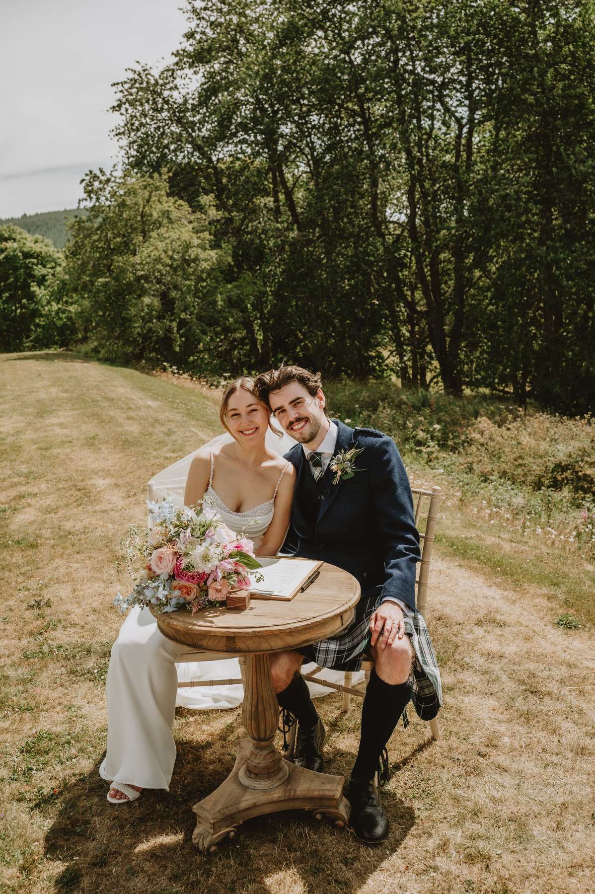 Newlyweds seated together to sign their wedding register in the grounds of Ballogie House