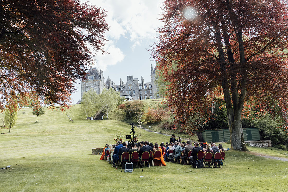 Outdoor wedding ceremony in the gardens of Atholl Palace Hotel with guests overlooking the historic Scottish castle venue
