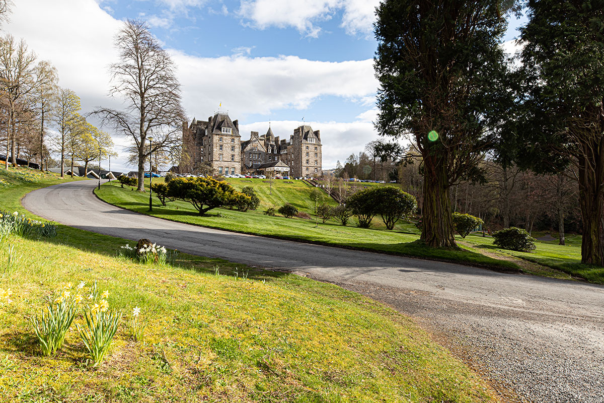 Atholl Palace Hotel in Pitlochry viewed from the winding driveway, with landscaped gardens, mature trees and the historic castle-style hotel in the background