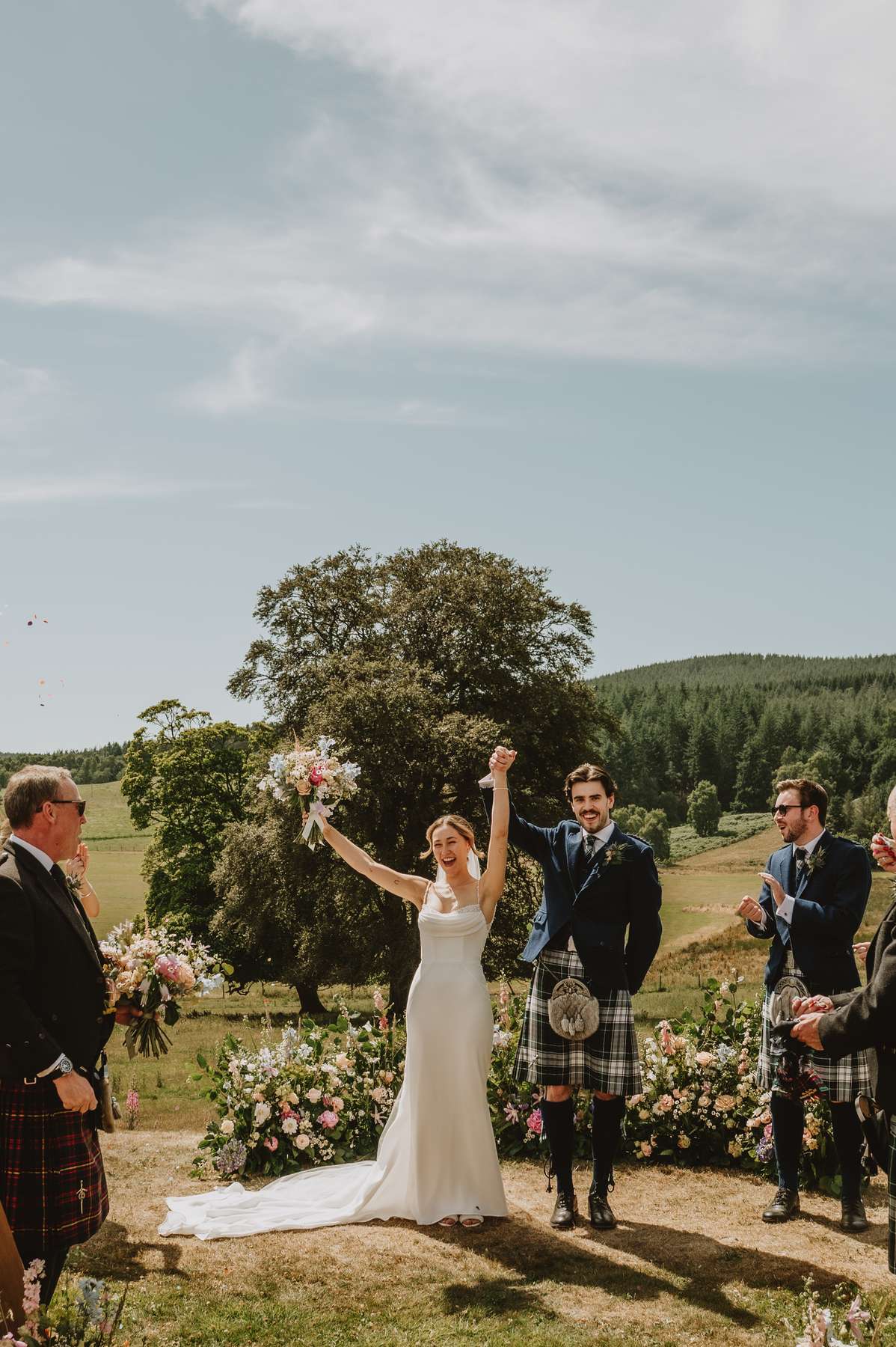 Newlyweds raise their hands in celebration after their outdoor wedding ceremony at Ballogie House