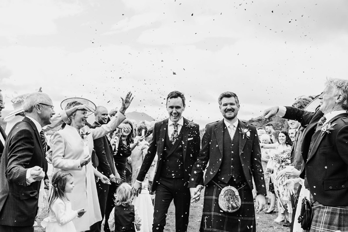 Black and white photo of grooms walking hand in hand through confetti