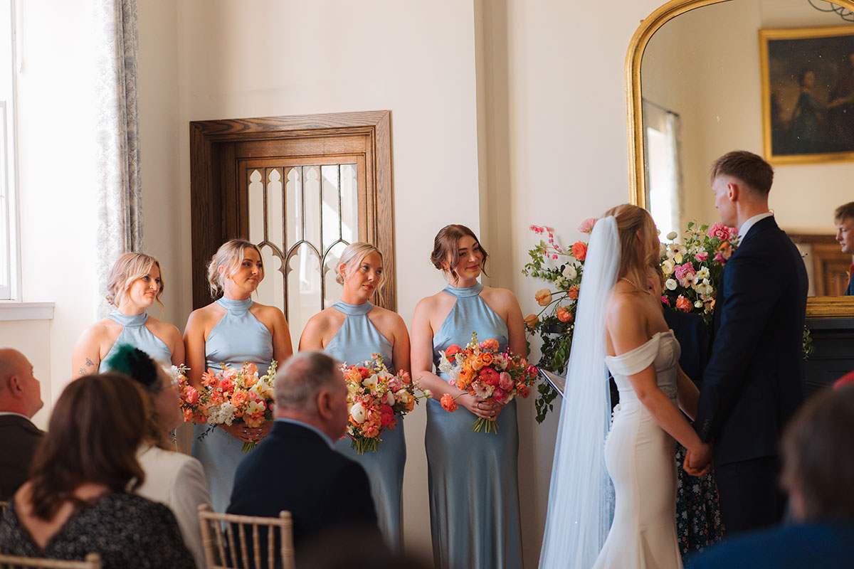 Bridesmaids in blue dresses holding colourful bouquets during indoor wedding ceremony