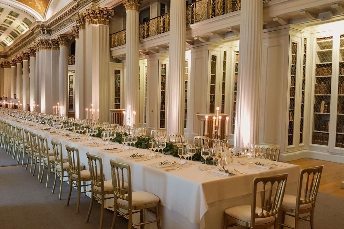 Elegant long-table wedding setup in The Signet Library with candlelight, greenery and classic gold chairs.