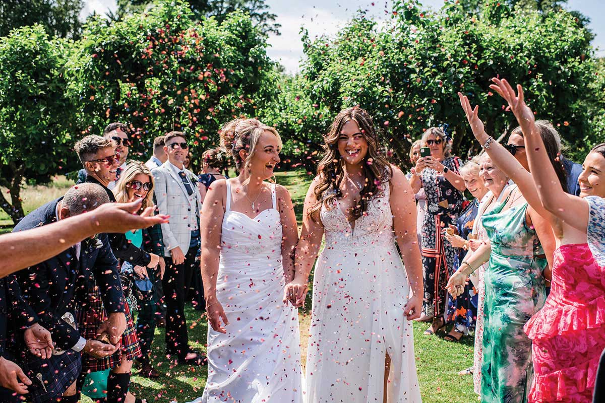 Couple walking through guests throwing confetti in the gardens at The Byre at Inchyra wedding venue in Perthshire.