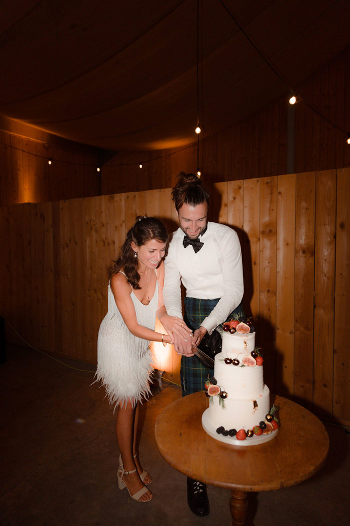 a bride and groom cutting a cake in the wedding barn at Carrick Castle Estate