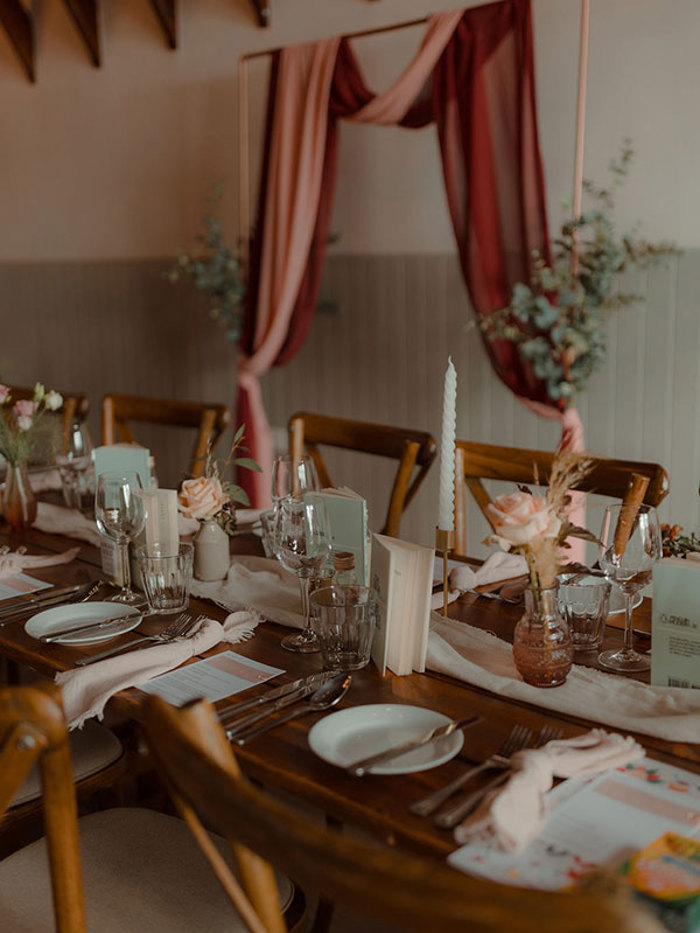 wooden dining table set with plates, cutlery, glassware, candle sticks, pale pink roses and small books