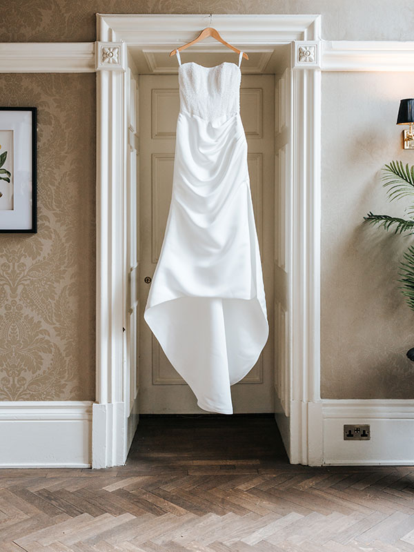 Strapless satin wedding dress hanging in a doorway during bridal preparations at Cornhill Castle
