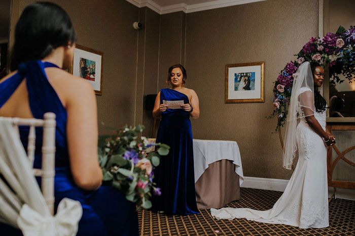 bridesmaid facing the room reading from a sheet of paper at wedding ceremony