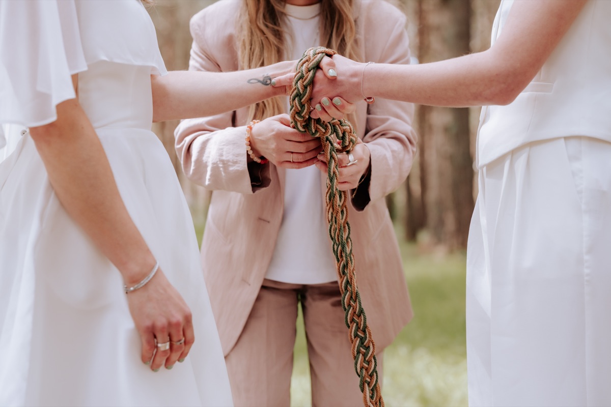 Close-up of Hannah and Donna’s hands being bound with a handfasting cord during their wedding ceremony.