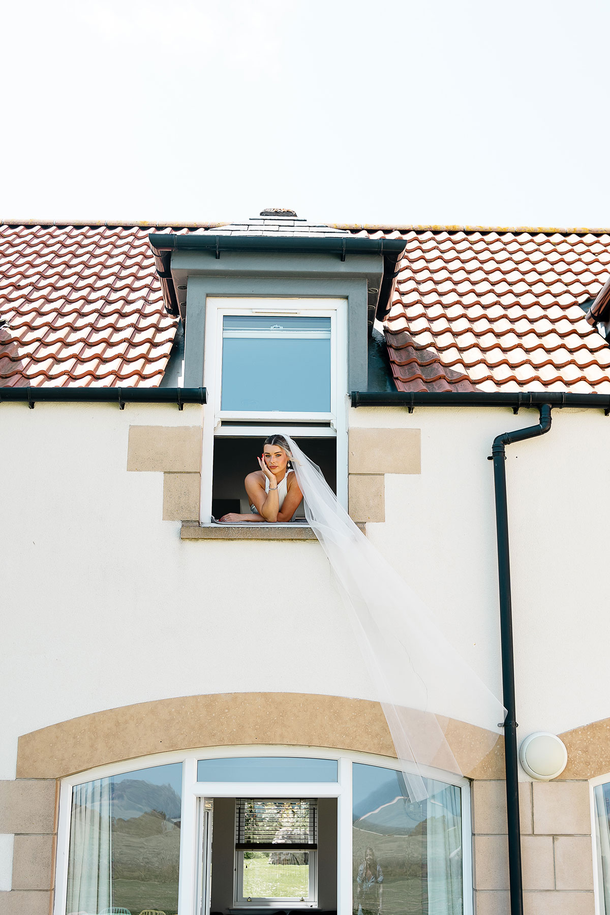 Bride leans from an upstairs window with her cathedral-length veil flowing down the front of the accommodation at Kinkell Byre.