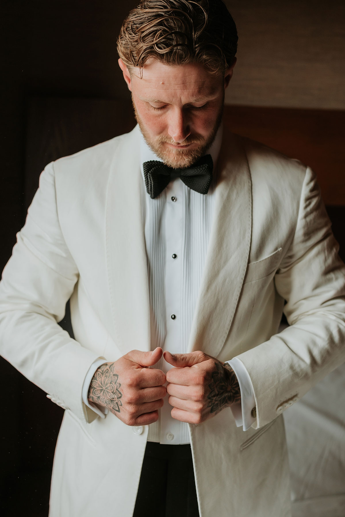 Groom adjusting white tuxedo jacket during wedding preparations at Ingliston Country Club