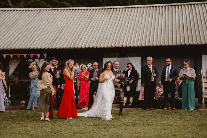 Bride and groom laugh while walking over grass surrounded by guests