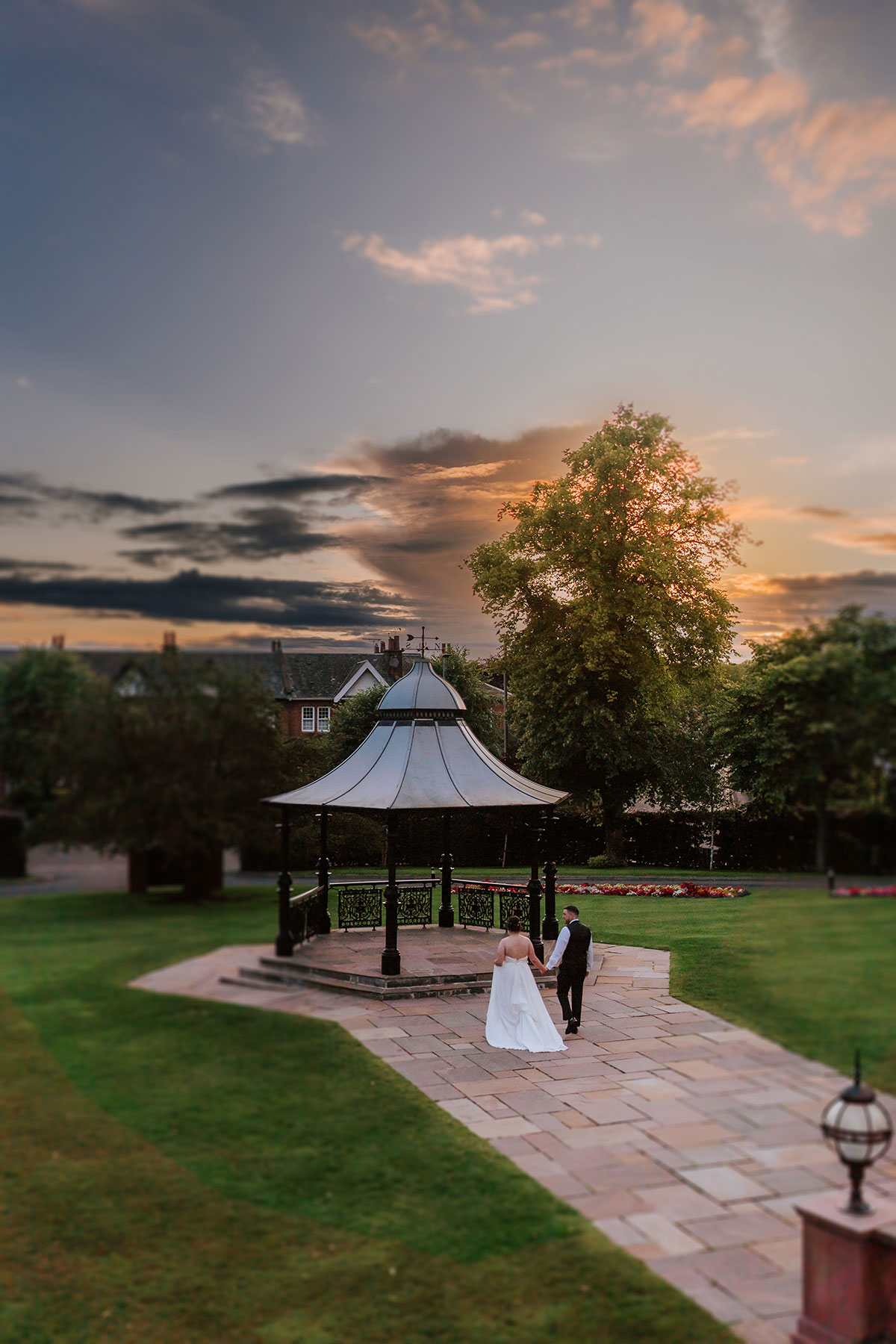Bride and groom walking hand in hand towards a bandstand at Boclair House at sunset, romantic Scottish wedding venue setting