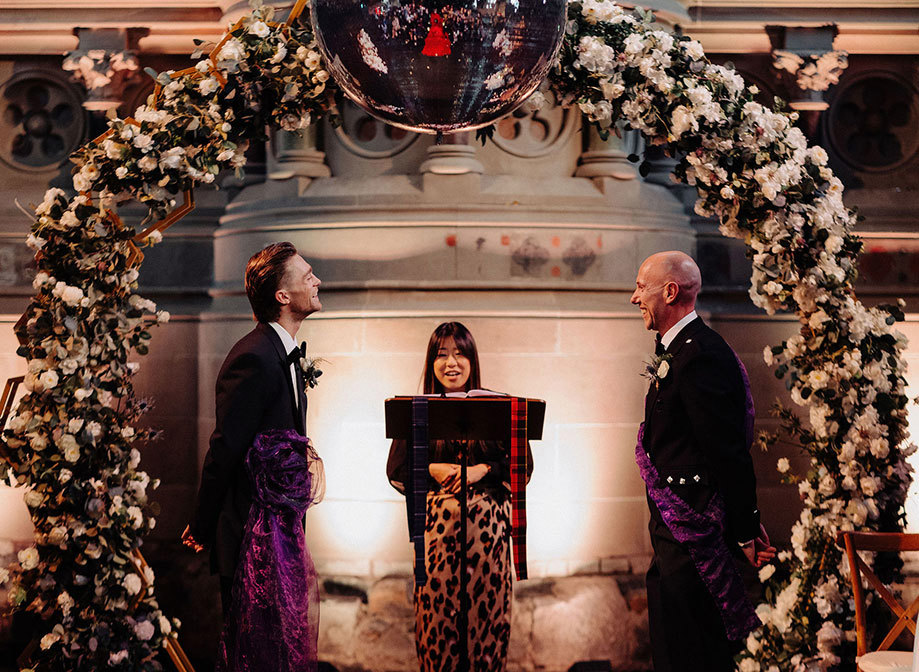 Two grooms With Celebrant Under Flower Arch