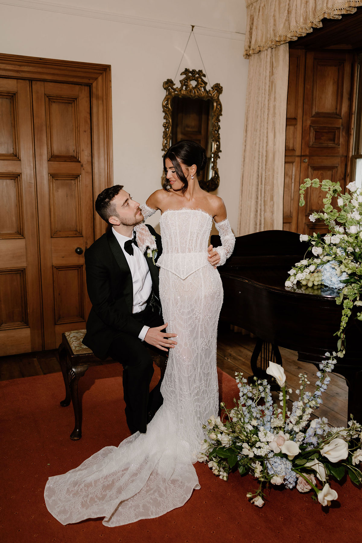 Bride and groom posing beside a grand piano surrounded by soft blue and white florals