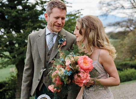 bride carries a colourful bouquet of flowers next to groom